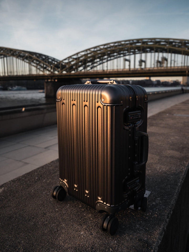 Traveler with a PREZOR suitcase in Metallic Grey by a bridge in the evening light