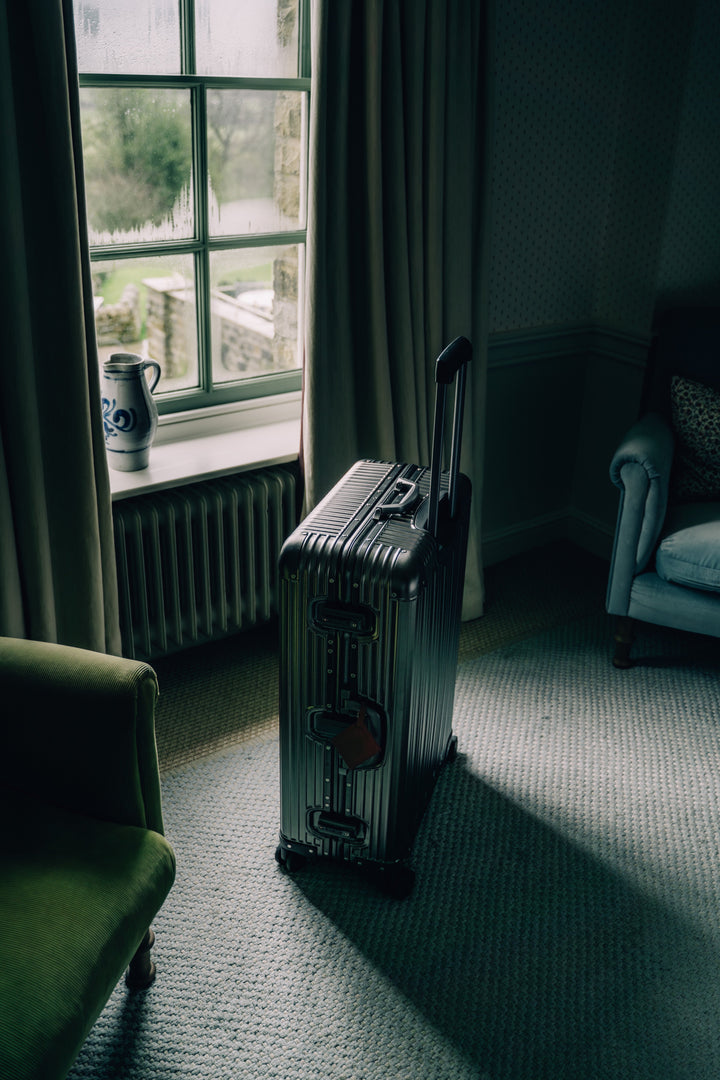 PREZOR suitcase in Metallic Grey at the window of a country house